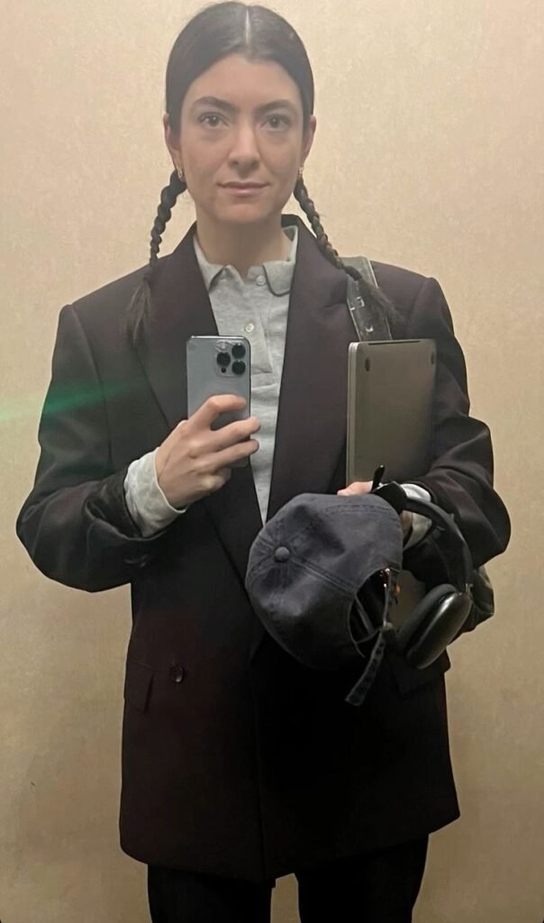 Lorde wearing a grey blazer and white shirt while holding a laptop — casual soft officecore look