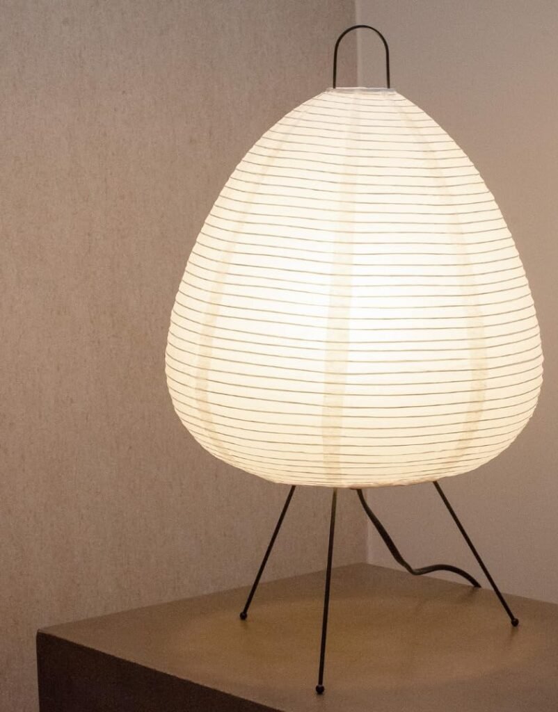 White paper lantern table lamp with black tripod legs on wooden side table