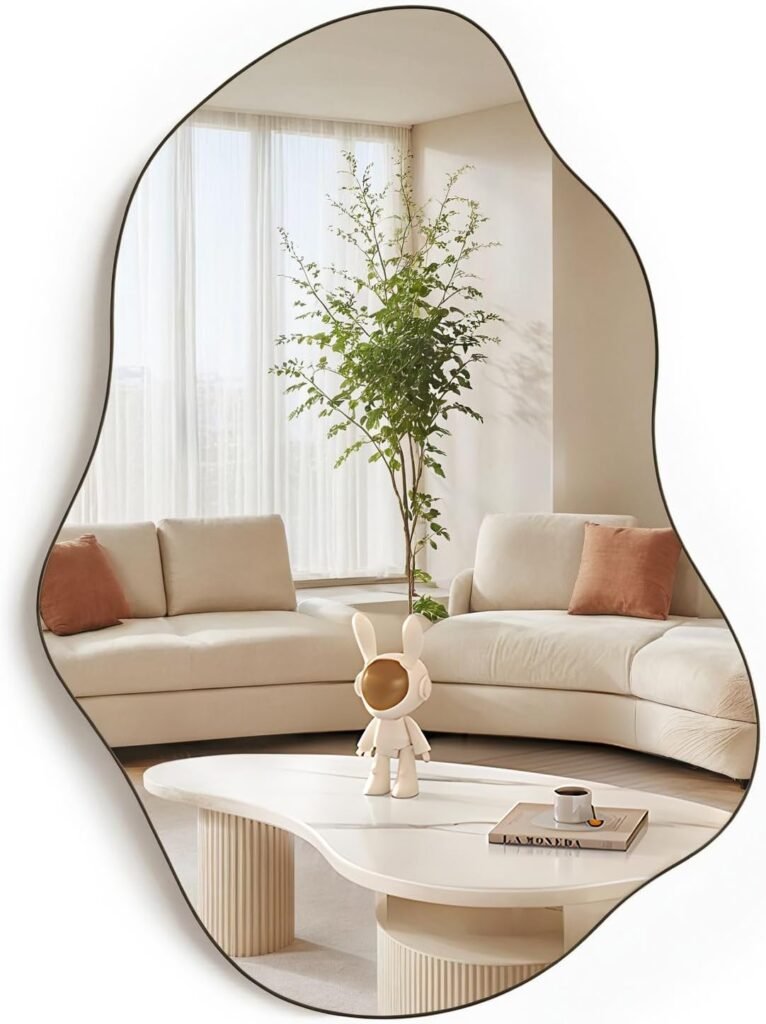 Large frameless asymmetrical wall mirror reflecting curved white sofa and indoor plant in neutral-toned room