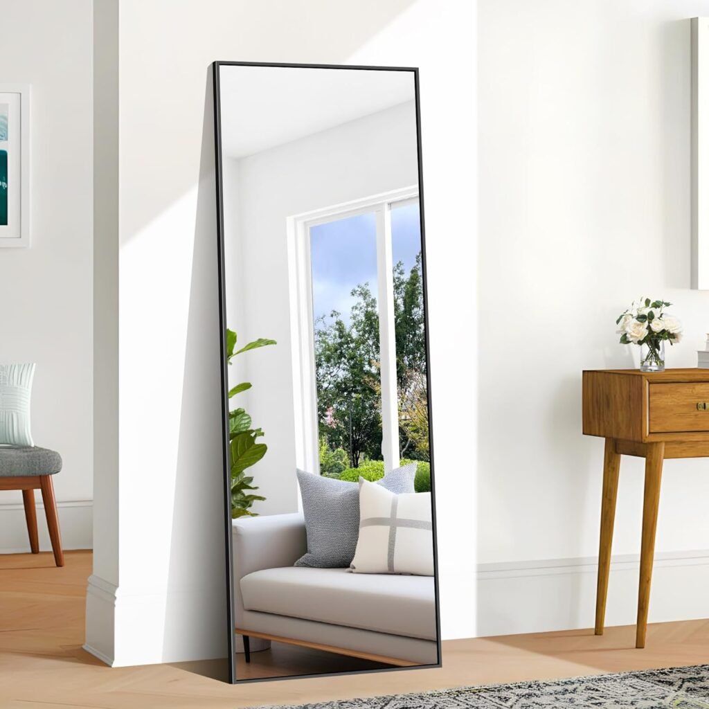 Full-length floor mirror with black frame leaning against white wall near wood console table