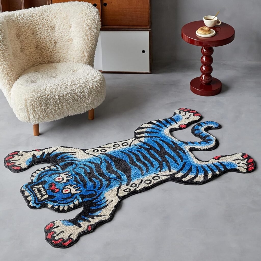 best rugs for your home - Blue tiger-shaped tufted rug on a grey floor next to a boucle chair and red accent table