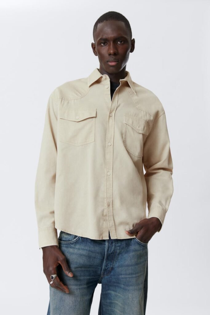 Model in a light beige long sleeve cotton twill shirt with chest pockets.