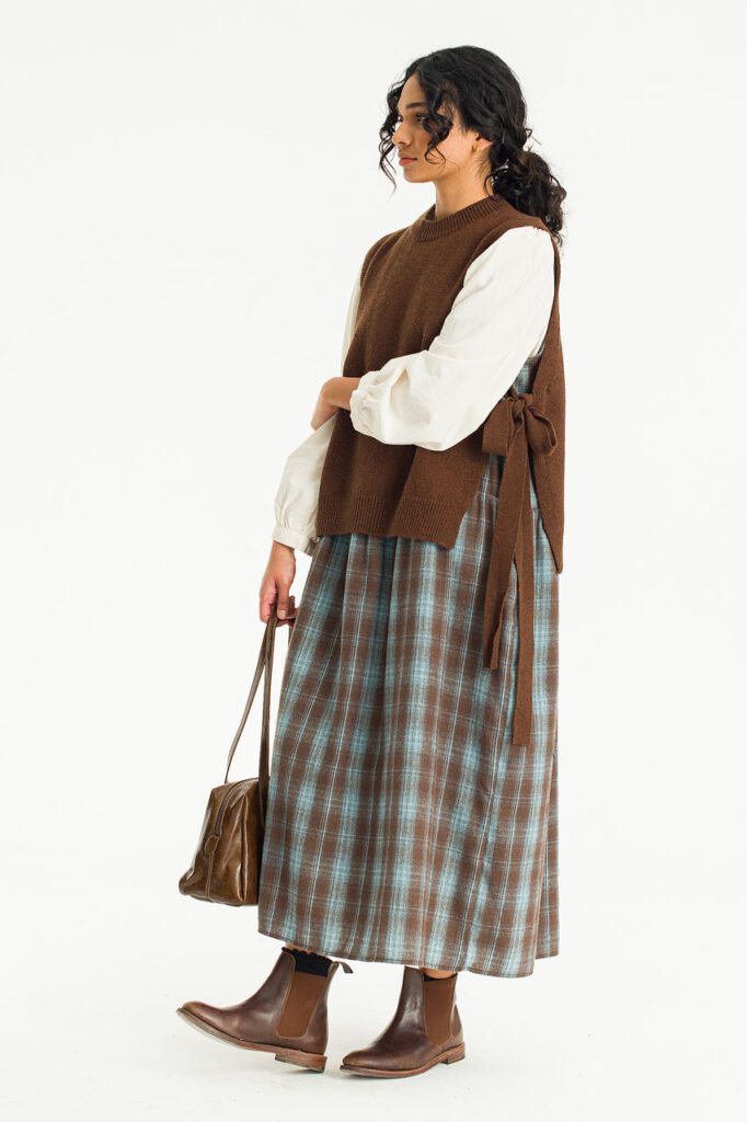 A side profile of a model wearing a brown knit vest with ribbon ties, styled over a puff sleeve dress.