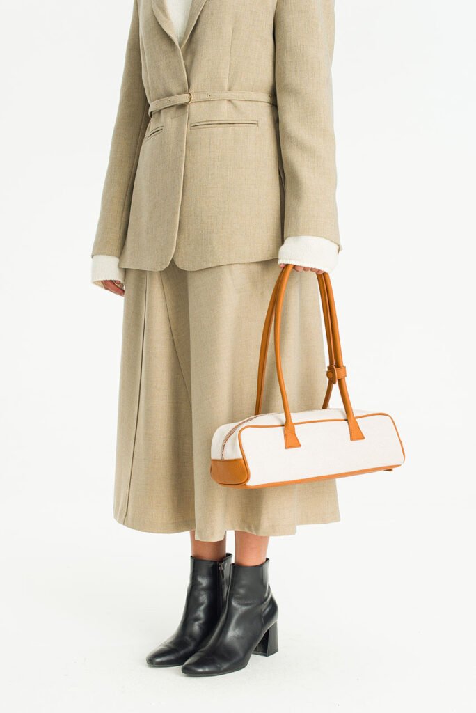 A close-up of a tan and white baguette-style shoulder bag from Olive Clothing, worn with a beige suit.