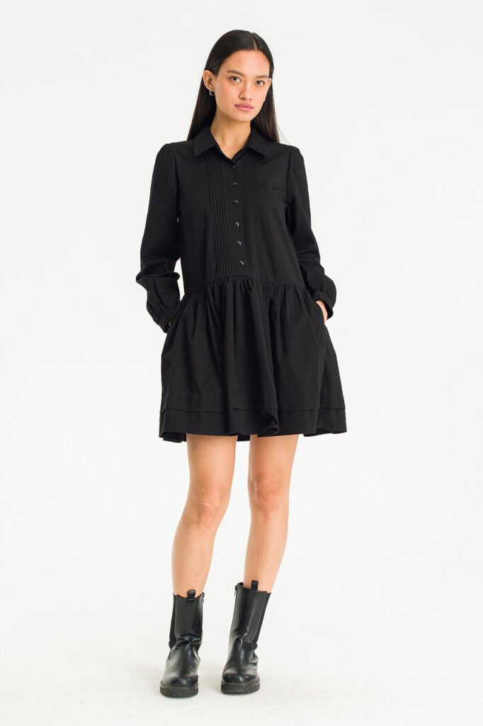A model wears a black long-sleeved pintuck mini dress from Olive Clothing, styled with black boots.