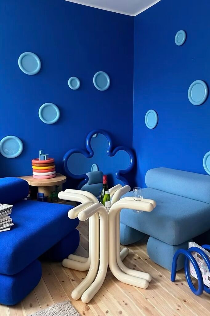 A saturated blue living room featuring rounded furniture, wall art, and a sculptural cream side table — classic Gustav Westman interior style. ikea x gustav westman