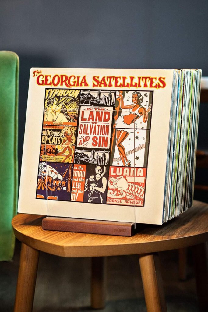 A compact vinyl record stand displaying albums on a small round wooden table beside a green velvet couch.
