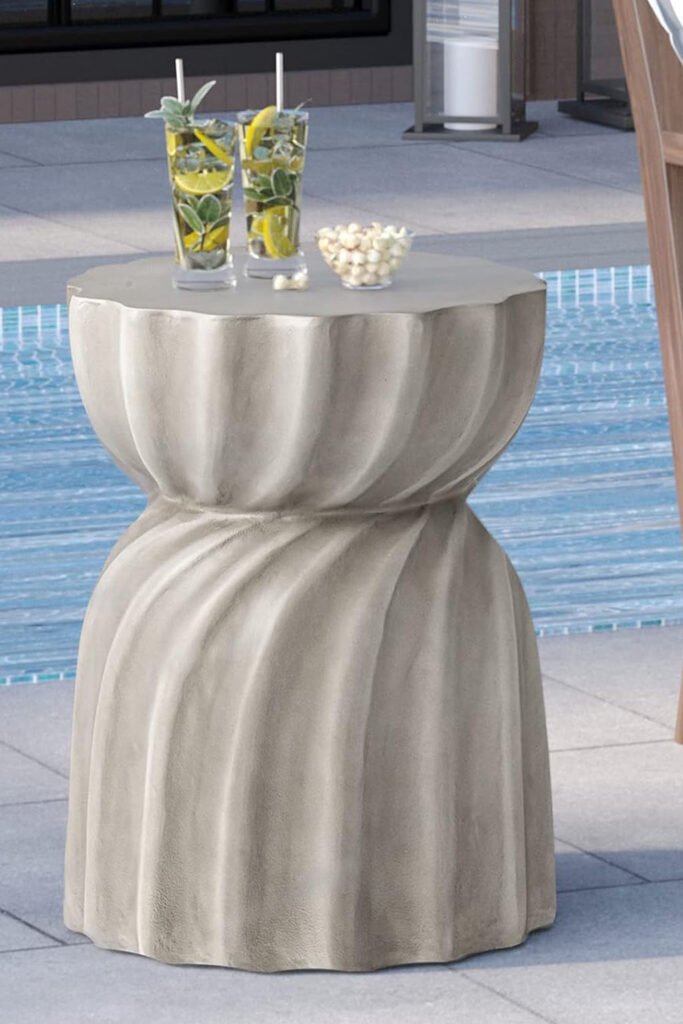 Outdoor-friendly side table with a twisted concrete shape, placed beside a striped lounger and a pool.
