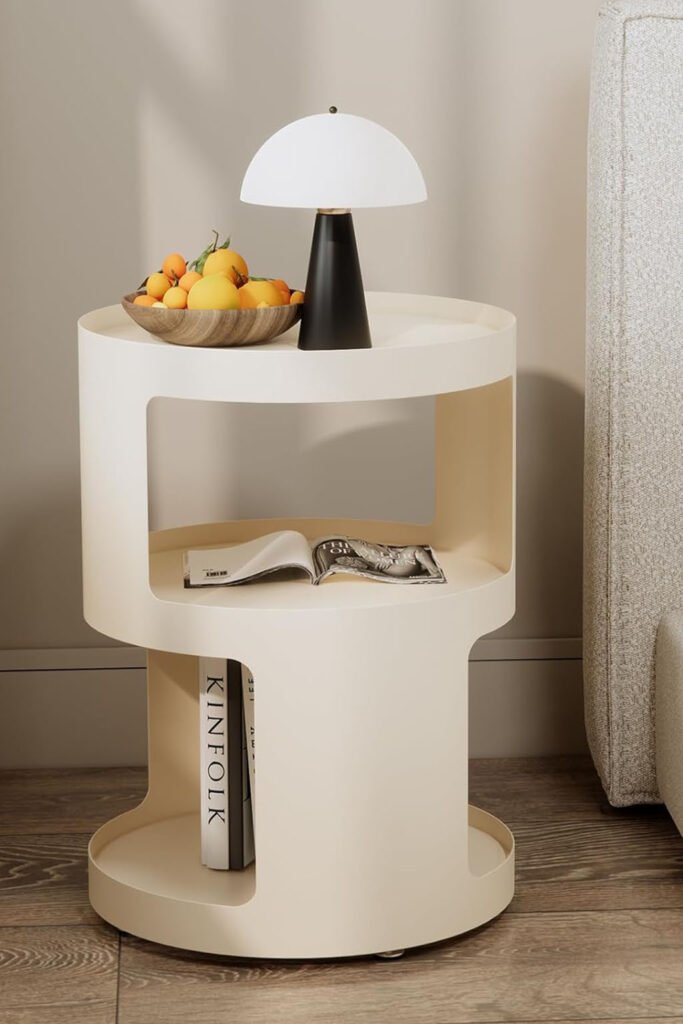 Minimalist white side table with three levels and rounded shelves, styled with a dome lamp and fruit bowl beside a modern bed.