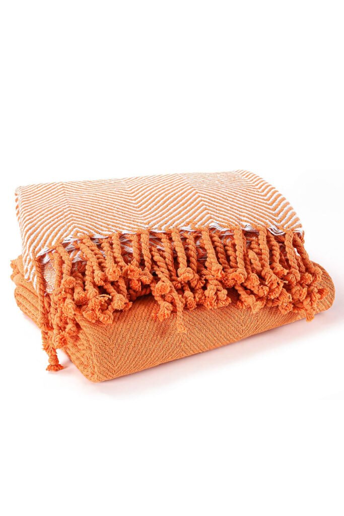 Folded orange and white herringbone throw blanket with thick fringe tassels
