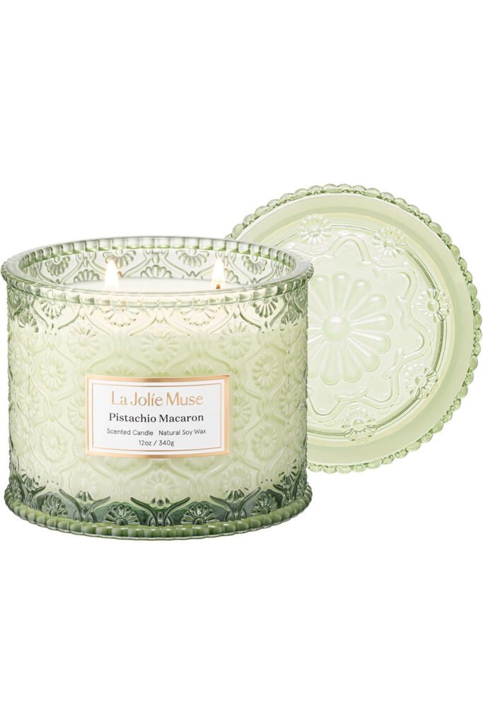 Green glass candle with embossed floral pattern and lit wicks.