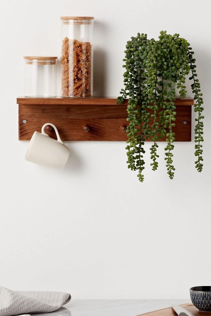 Wooden wall shelf with glass jars, a ceramic mug, and a trailing plant styled against a white wall.